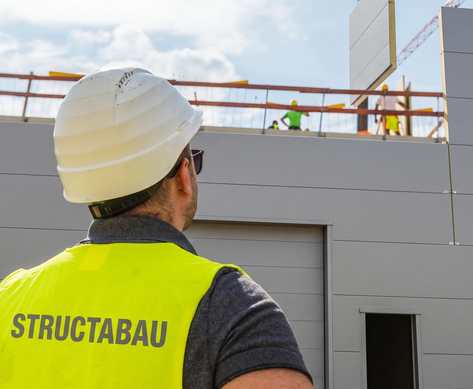 Bauleiter mit Structabau-Weste vor einem laufenden Hochbauprojekt